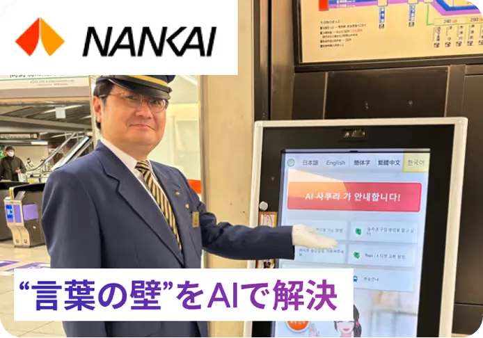 南海電鉄の駅に設置されたAIさくらさんのサイネージと、その横に立つ駅係員